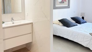 A modern bathroom with a white sink and mirror, and a bedroom with a bed, pillows, and a framed picture on the wall. - Unique in St Cyprien, right on the water (Saint-Cyprien)