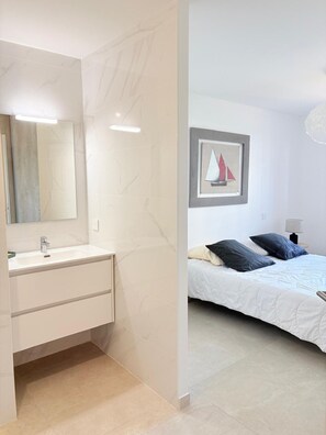 A modern bathroom with a white sink and mirror, and a bedroom with a bed, pillows, and a framed picture on the wall. - Unique in St Cyprien, right on the water (Saint-Cyprien)