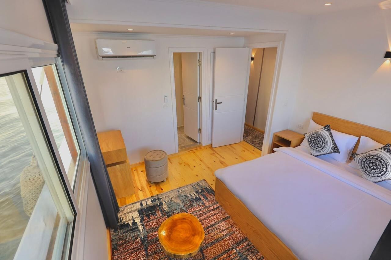 Habitación de hotel moderna con una cama grande, una mesita auxiliar pequeña, una lámpara de noche y vistas a través de una ventana.