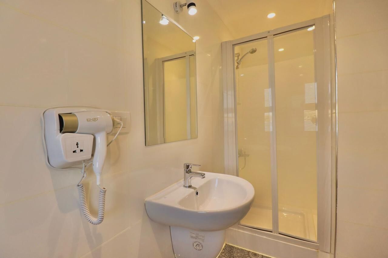 Un baño con lavamanos blanco, espejo y ducha con mampara de vidrio.