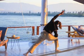 A person performing a yoga pose on a deck with a view of a calm body of water and distant mountains.