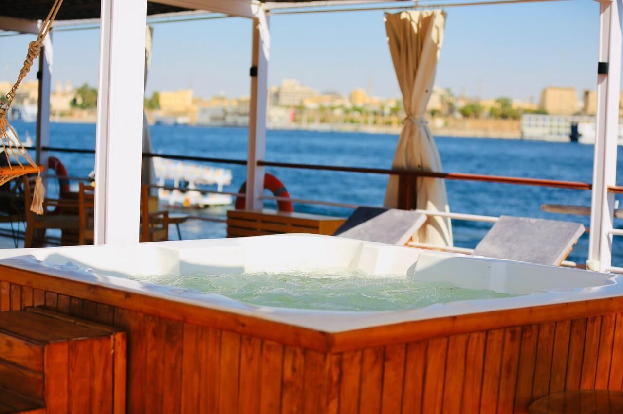 Una bañera de madera en la cubierta de un barco, con vistas al mar y un paisaje urbano al fondo.