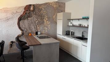 Eine moderne Küche mit einer zentralen Kochinsel, weißen Schränken und einer Wand mit einer besonderen Struktur.