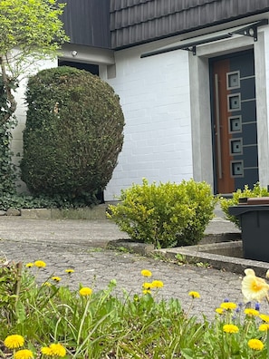 Ein modernes Gebäude mit weißer Fassade, einer großen Hecke und einer Tür mit geometrischem Design.