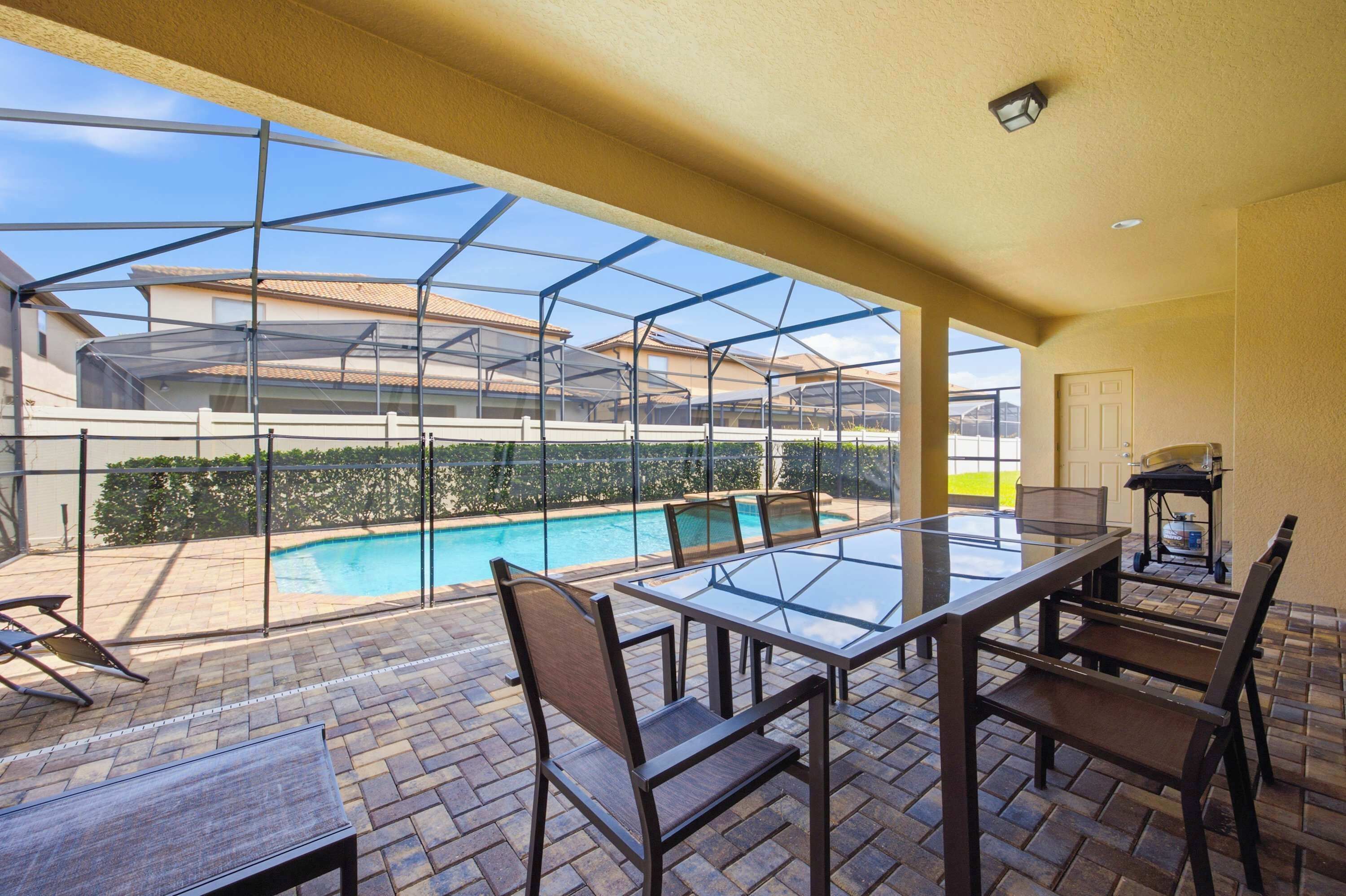 Un espacio al aire libre techado con piscina, mesa de vidrio, sillas y una parrilla.
