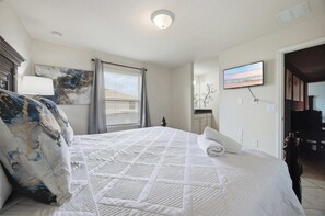 Hotellihuone, jossa on sänky, taulu, televisio ja kylpyhuone, joka näkyy avoimesta ovesta.