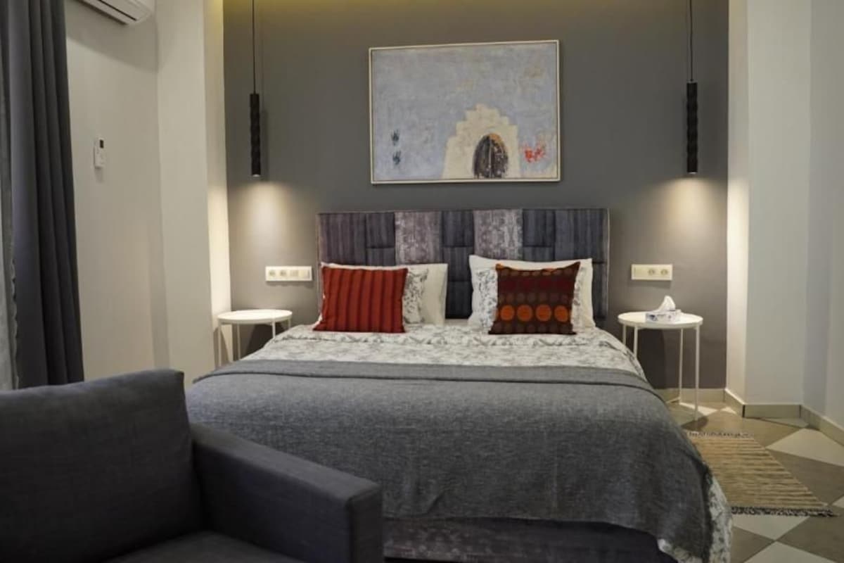 A modern bedroom with a large bed, two bedside tables, a chair, and a wall-mounted artwork.