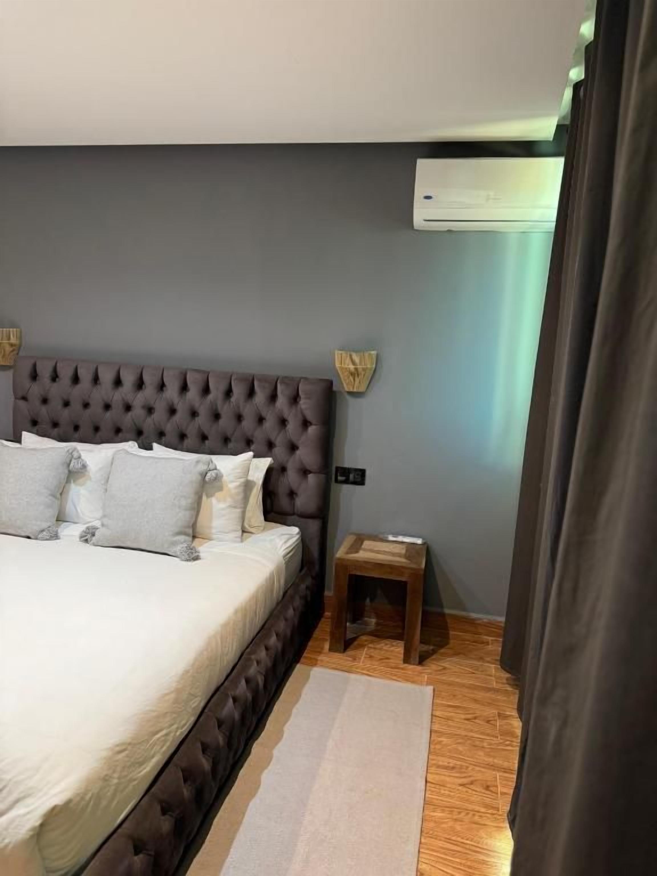 Un dormitorio con cabecera capitonada, una mesita de noche y un aire acondicionado de pared.