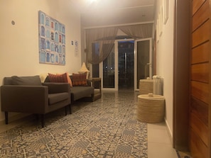 Una sala de estar con dos sofás, baldosas estampadas en el suelo, una pared con un mural azul y blanco, y un ventanal corredero que da a un área exterior.