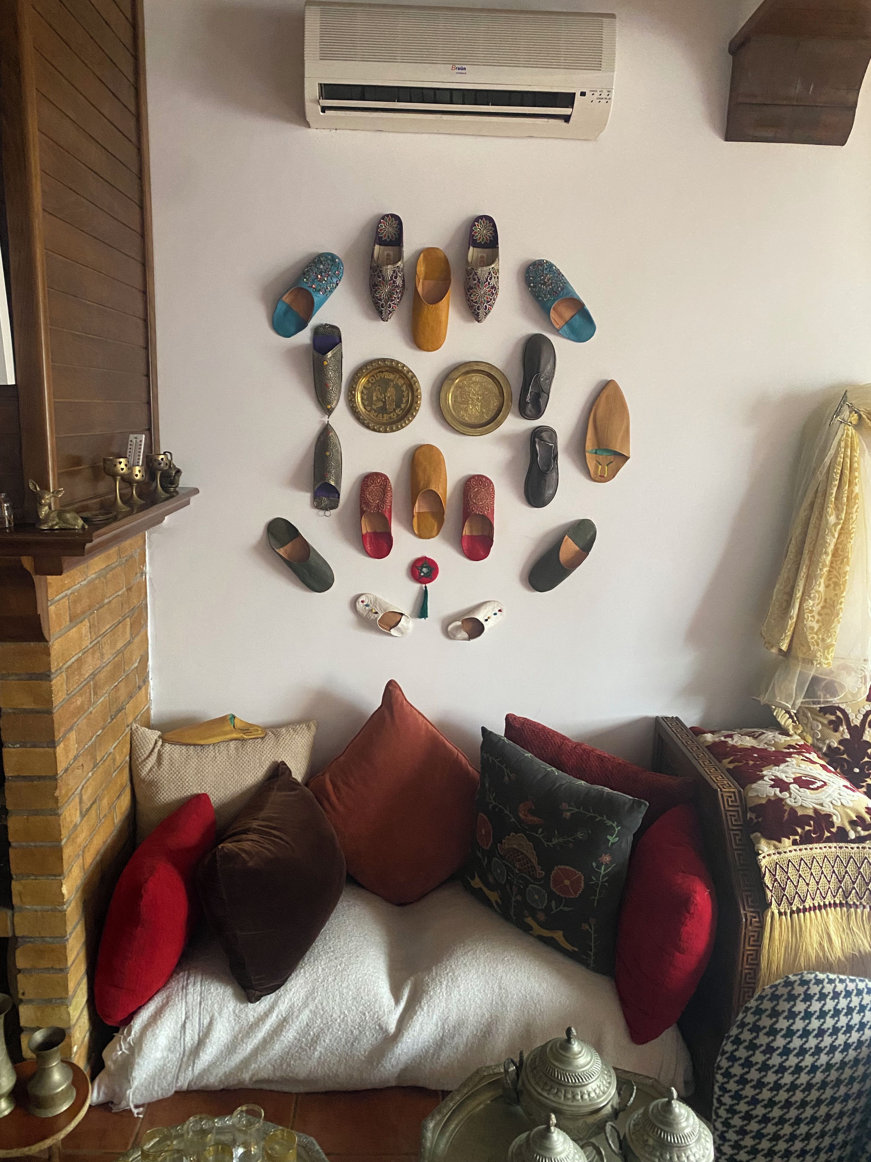 Habitación con zapatero de pared, chimenea de ladrillo, sofá con cojines y manta estampada.