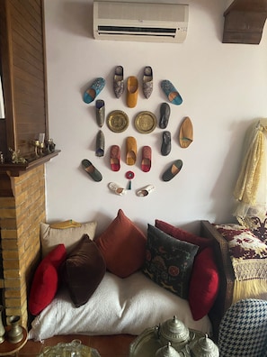 A room with a wall-mounted shoe display, a brick fireplace, a sofa with cushions, and a patterned throw.