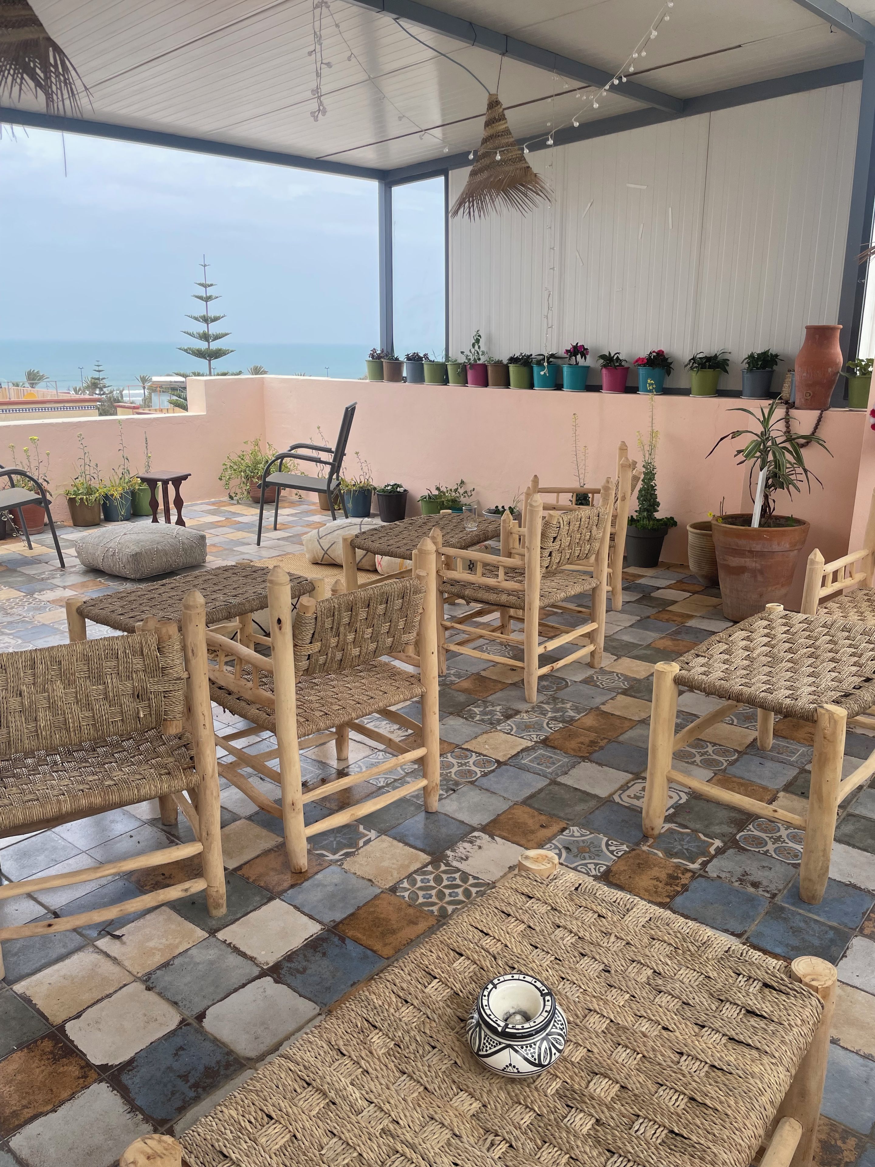 Una terraza con mobiliario de mimbre, plantas en macetas y vista al mar.