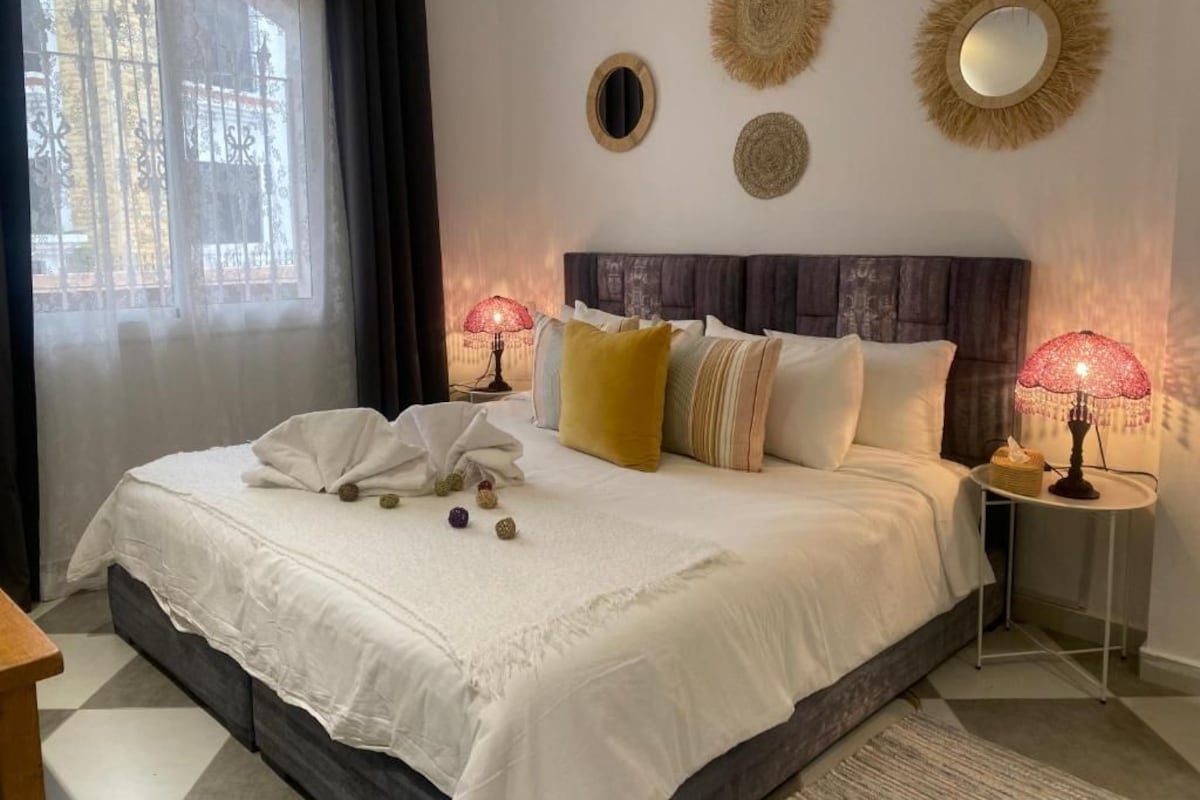 A bedroom with a large bed, two bedside lamps, and decorative wall mirrors.