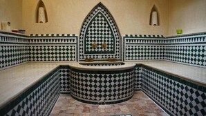 Um quarto com piso xadrez, um nicho central com arco decorativo e duas pequenas áreas de parede embutidas.
