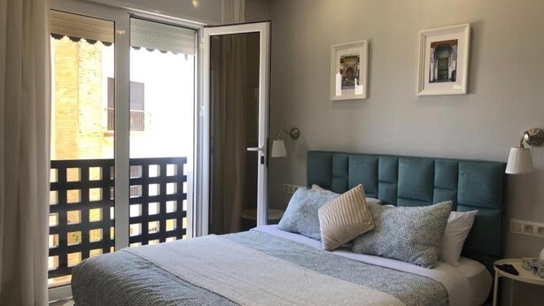 A bedroom with a bed, a nightstand, a lamp, and a view through a sliding door.