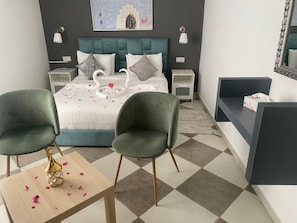A modern bedroom with a bed, two green chairs, a bedside table with a decorative item, and a nightstand with a lamp. - Riad Casa Bahia (Asilah)