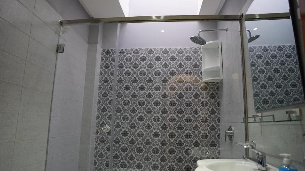 Una ducha con puerta de vidrio, un lavabo con espejo y baldosas estampadas en las paredes.
