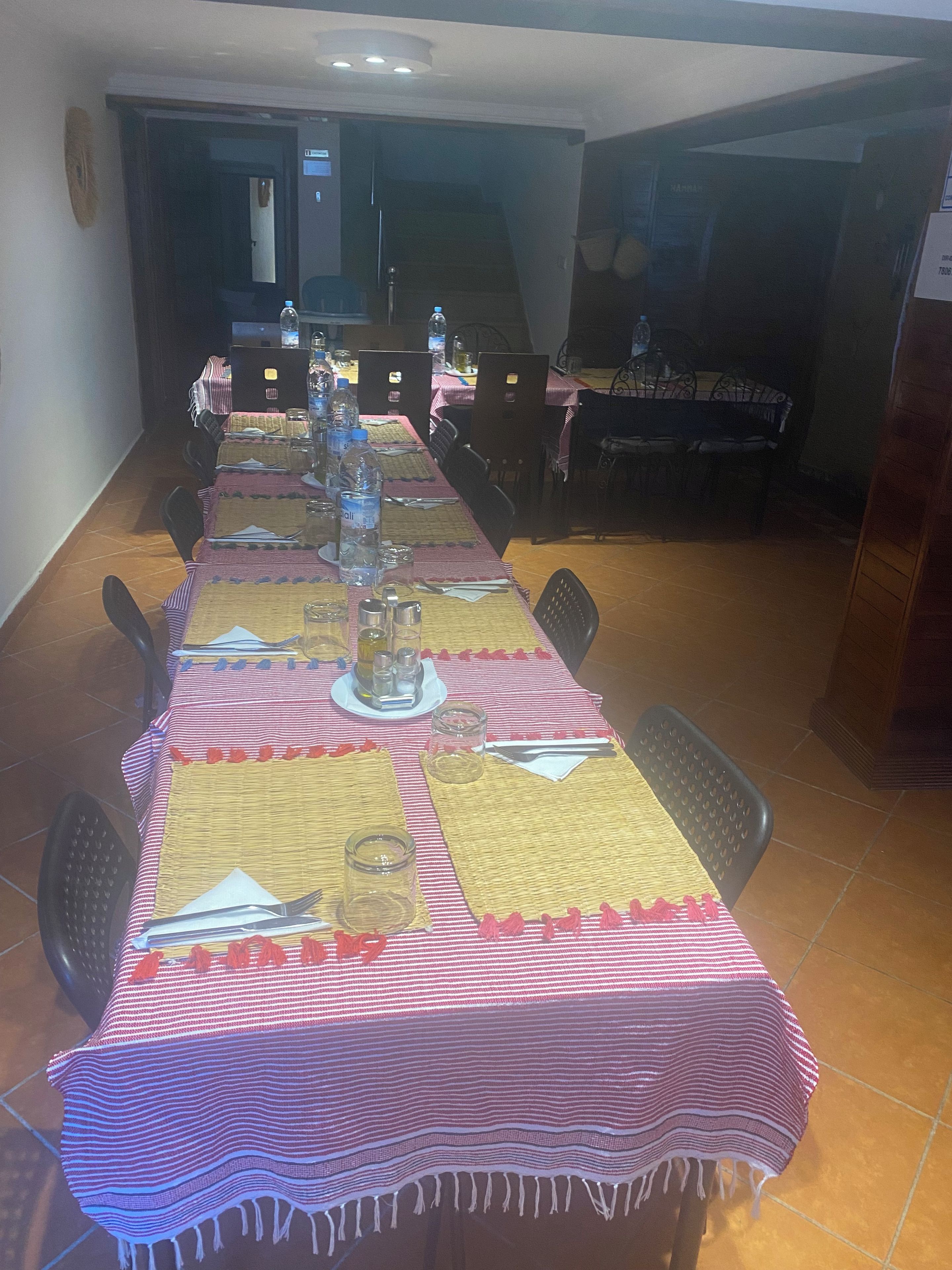 A dining area with a long table set for a meal, chairs around it, and a kitchen in the background.