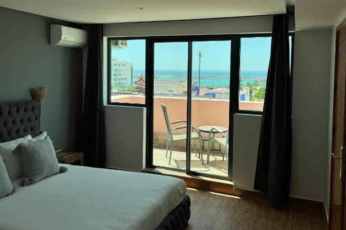 A hotel room with a large bed, a view of the beach, and a sliding glass door to the balcony.