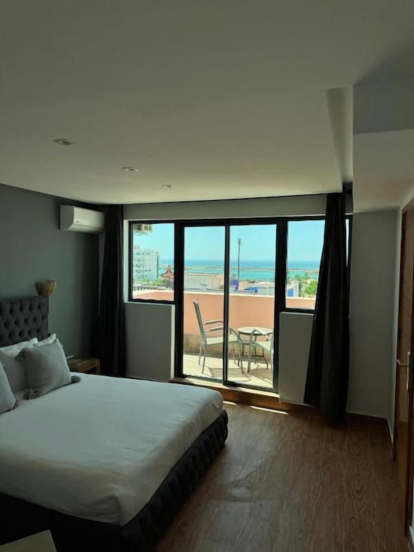 A hotel room with a large bed, a view of the beach, and a sliding glass door to the balcony.