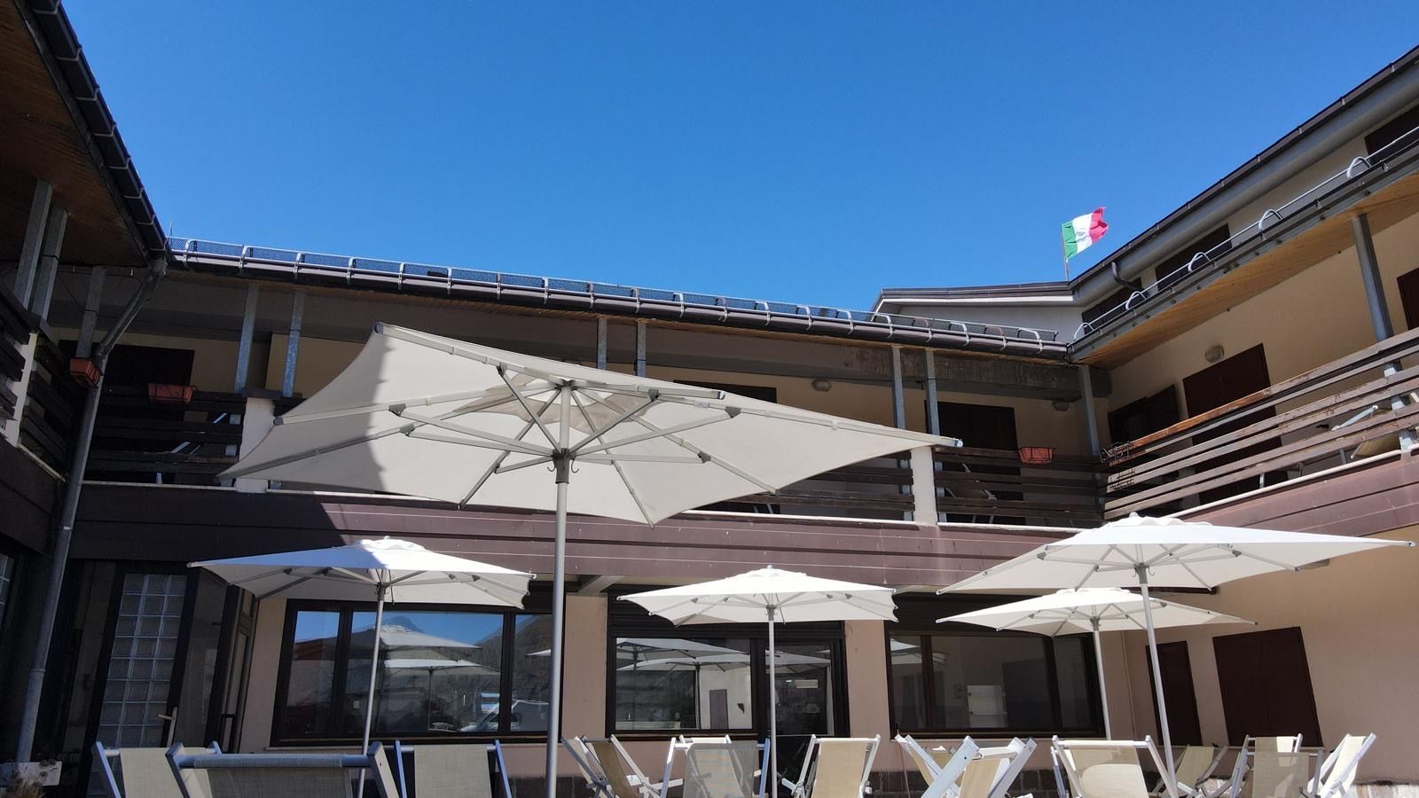 A building with outdoor seating under umbrellas, a balcony, and a flag.