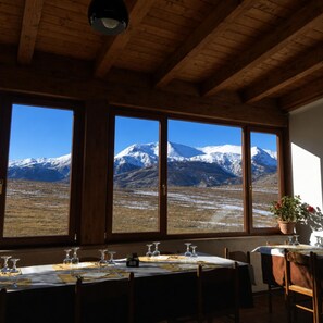 A dining area with a table set for four, large windows with a mountain view, and wooden ceiling beams.