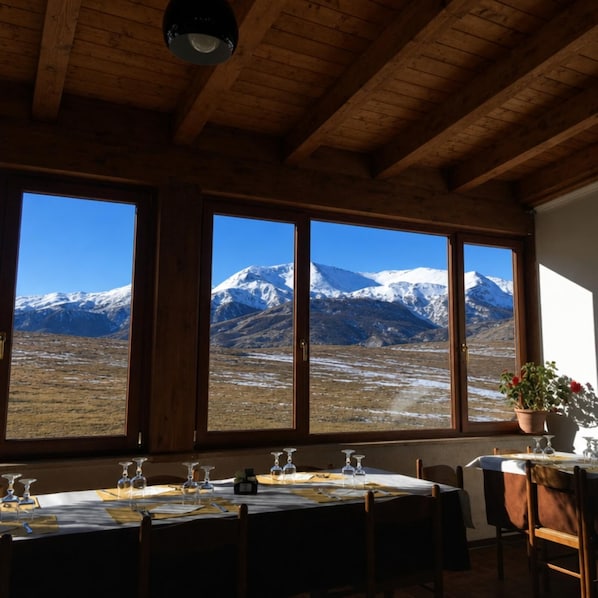 A dining area with a table set for four, large windows with a mountain view, and wooden ceiling beams.