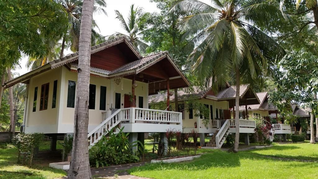 A row of bungalow-style accommodations with balconies, surrounded by lush greenery and palm trees.