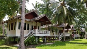 A row of bungalow-style accommodations with balconies, surrounded by lush greenery and palm trees.