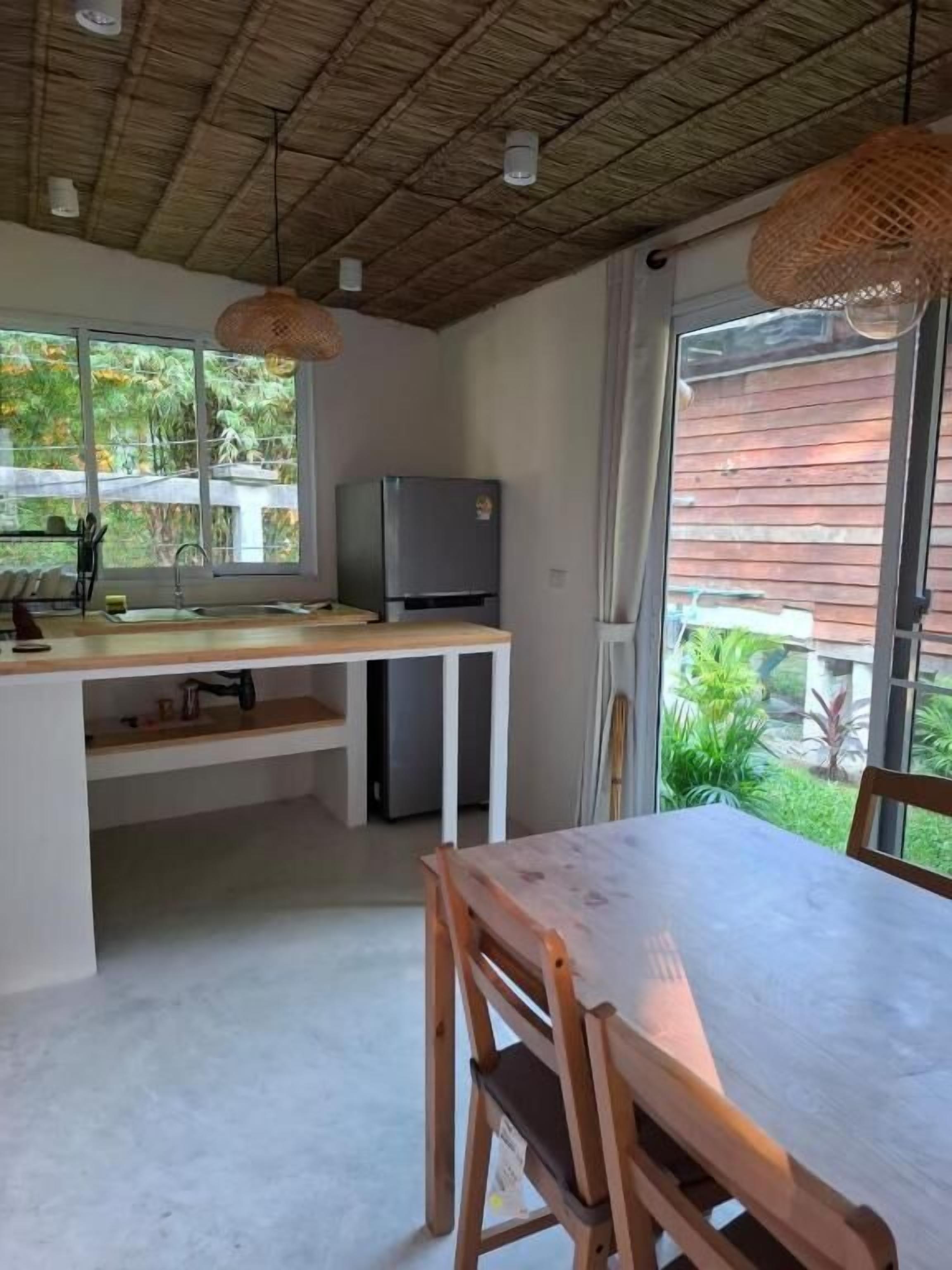 A kitchen with a dining table and chairs, a refrigerator, and a window with a view of greenery.