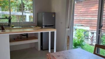 A kitchen with a dining table and chairs, a refrigerator, and a window with a view of greenery.