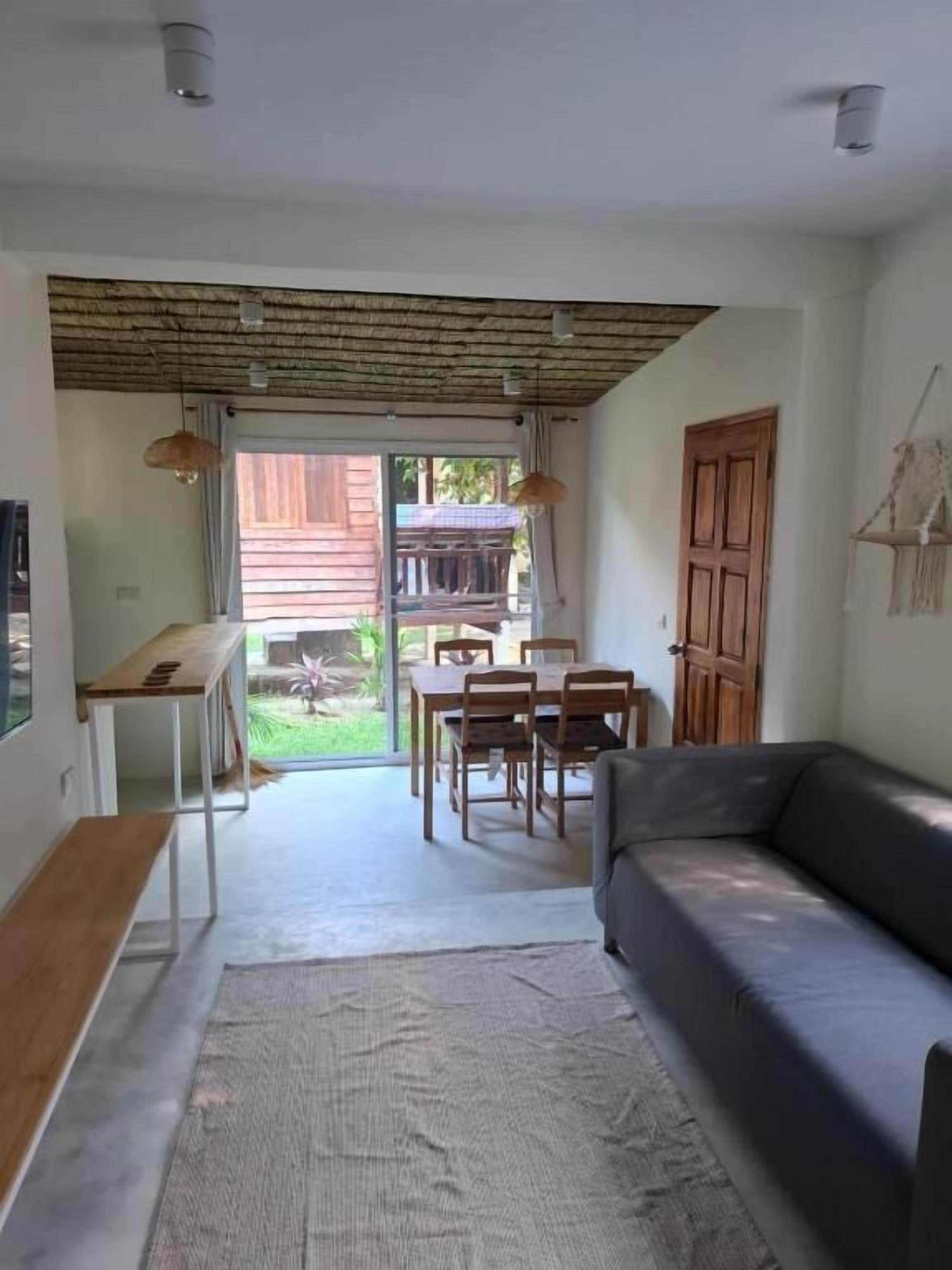 Una sala de estar con sofá, una mesa de comedor, sillas y un banco. Hay una puerta que da a un área exterior.