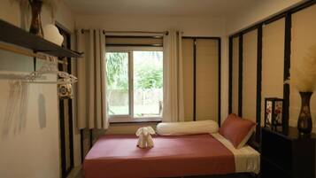 A hotel room with a bed, a window with curtains, a bedside table, and a shelf with decorative items.
