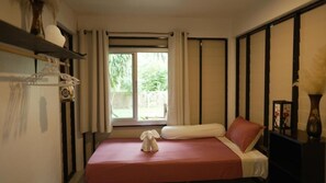 Una habitación de hotel con una cama, una ventana con cortinas, una mesita de noche y un estante con objetos decorativos.