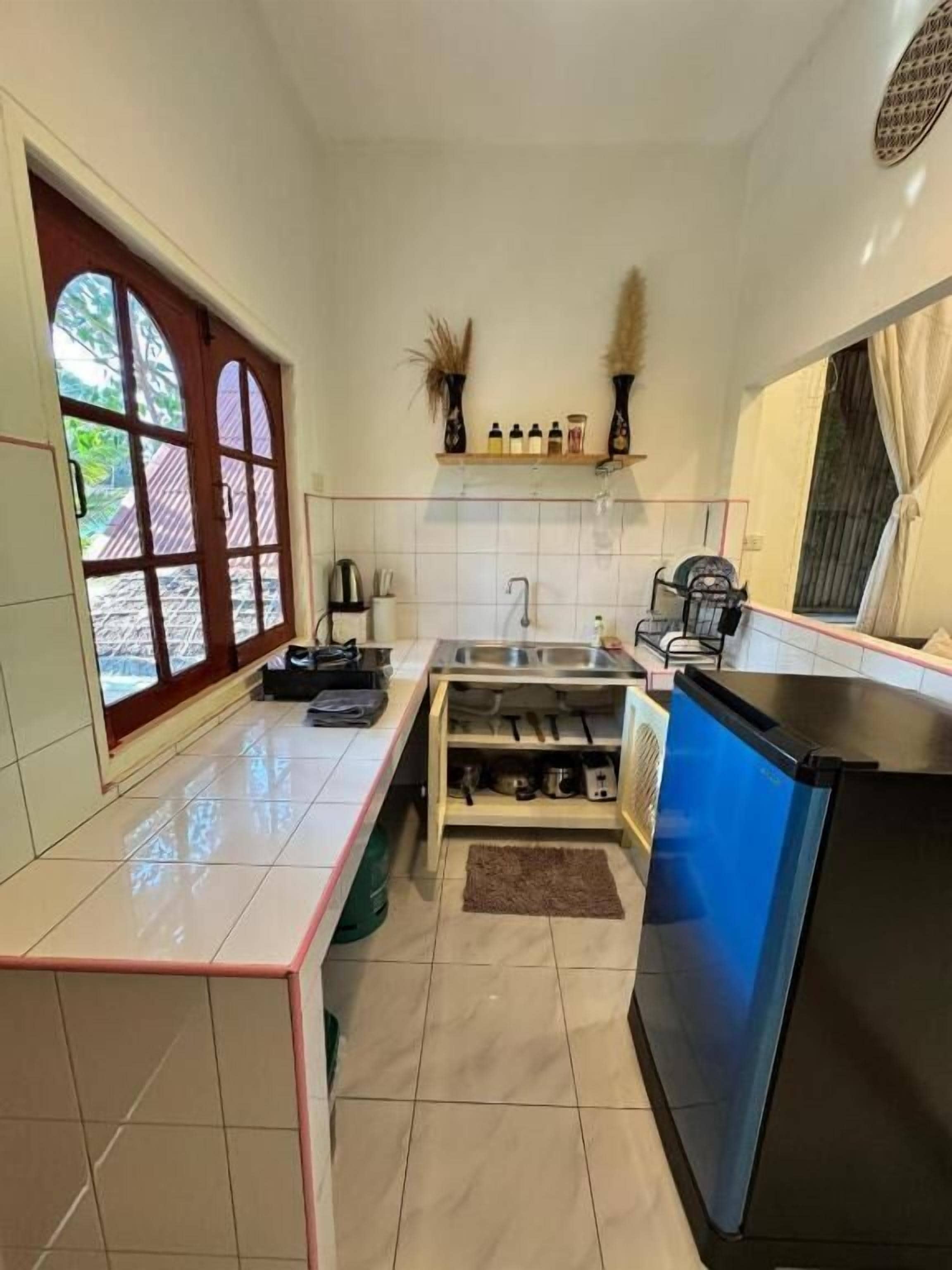 Una cocina con un ventanal amplio, un lavabo, un refrigerador negro y una encimera con varios objetos.