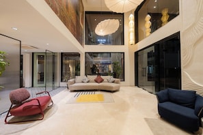 A spacious living area with a sofa, a red chair, and a blue sofa. There is a large window and a ceiling light fixture. - The Stories - DLF Road, Gachibowli (Hyderabad)