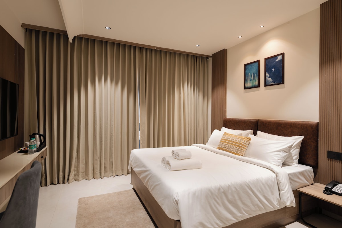 A hotel room with a large bed, a bedside table with a phone, and a wall-mounted TV.