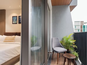 A modern hotel room with a bed, a grey armchair, a small wooden table, and a potted plant. - The Stories - DLF Road, Gachibowli (Hyderabad)
