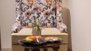 Une pièce comprenant un fauteuil à motifs floraux, une petite table avec des fruits et un vase avec une plante.