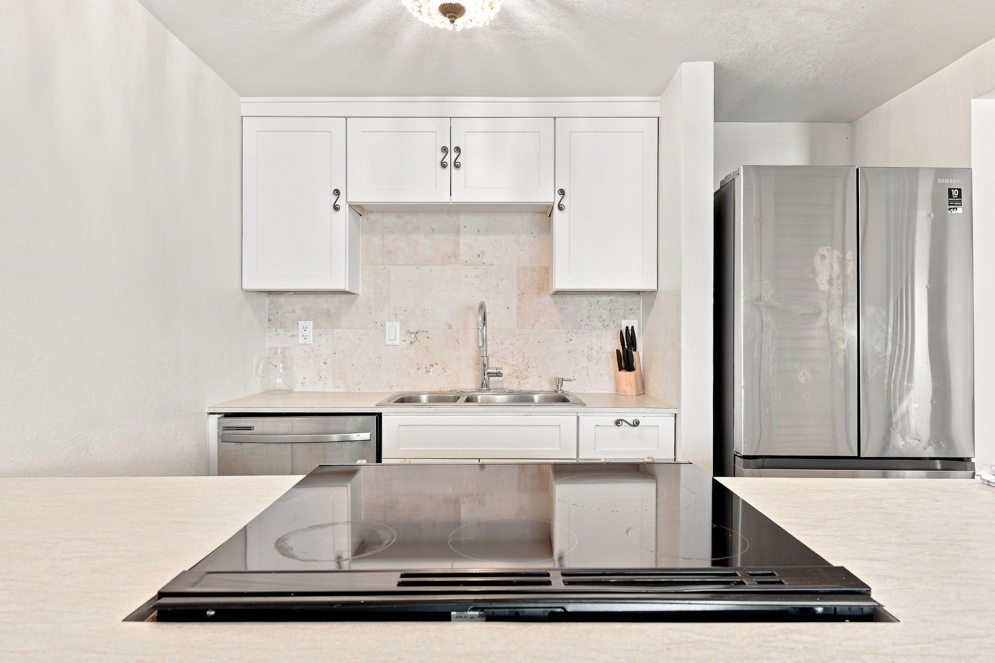 Une cuisine moderne avec des meubles blancs, des appareils en acier inoxydable et une plaque de cuisson à induction noire.