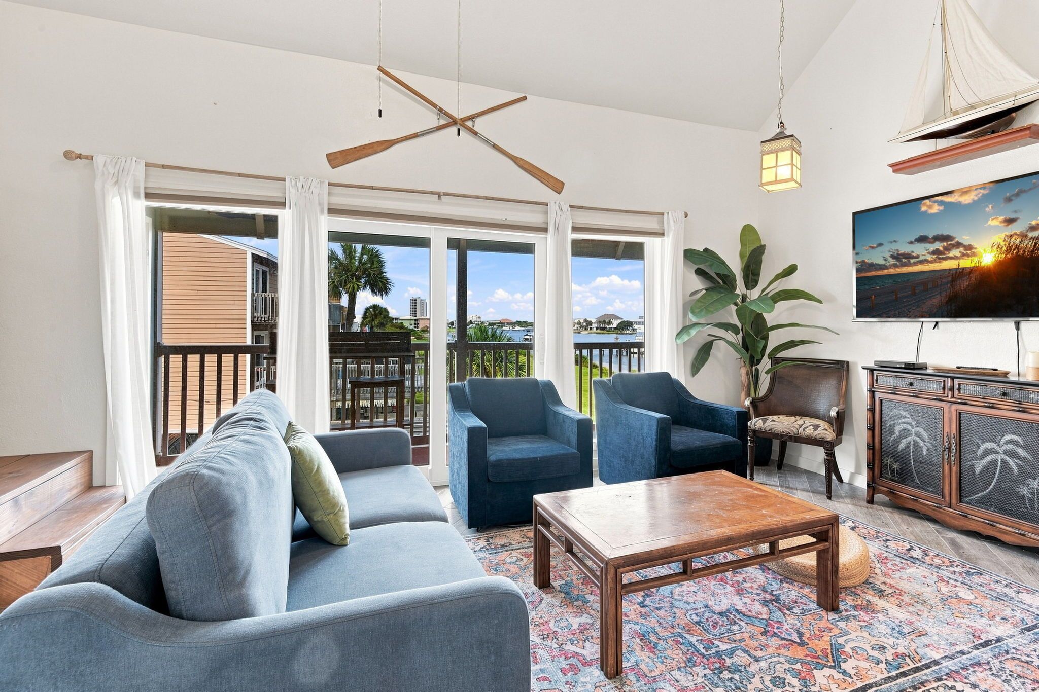 A spacious living room with a blue sofa, two armchairs, a coffee table, and a TV mounted on the wall.