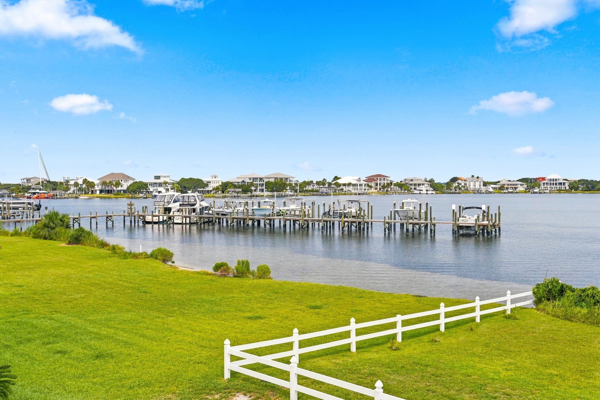 A marina with boats docked, a white fence, and houses in the background.
