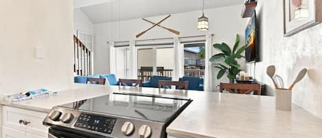 Une cuisine moderne avec un îlot central, un coin repas avec des chaises bleues et une vue sur l’extérieur.