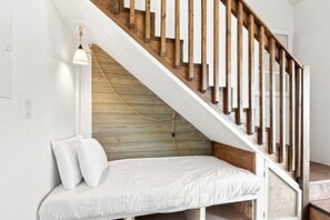 Eine Holztreppe mit Geländern führt zu einem Schlafzimmer auf dem Dachboden, ausgestattet mit einem weißen Bett und Kissen.