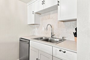 A modern kitchen with white cabinets, a stainless steel sink, and a dishwasher. - 🌊🏖️ Sand Dollar W-210 | Steps to Beach + Bunk Room | Pensacola Beach (Pensacola Beach)