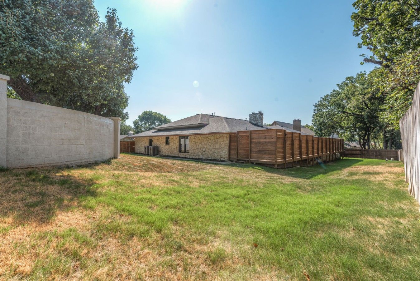 Une maison avec une façade en pierre, une terrasse en bois et une cour gazonnée.