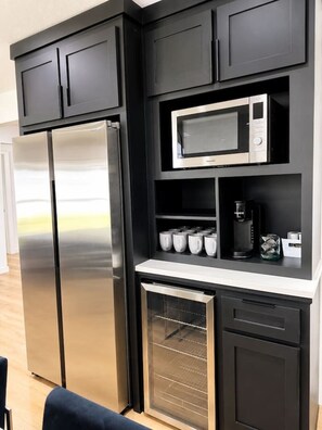 A modern kitchen with a stainless steel refrigerator, a microwave, and a coffee maker on the countertop. - Luxury South Tulsa Retreat | 4 King Beds • Hot Tub (Tulsa)