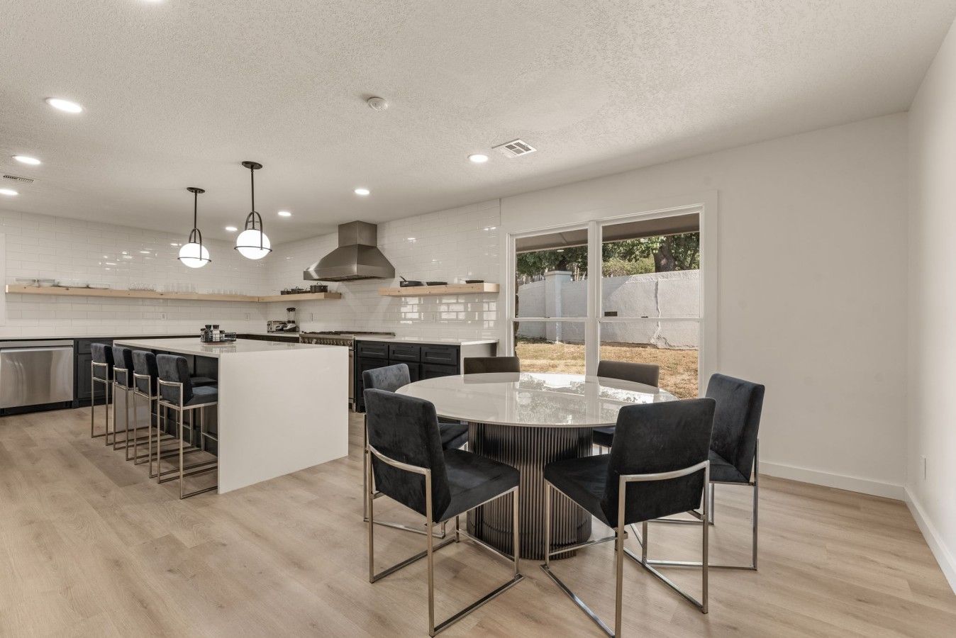 A modern kitchen with a central island, bar stools, and a dining table with chairs.