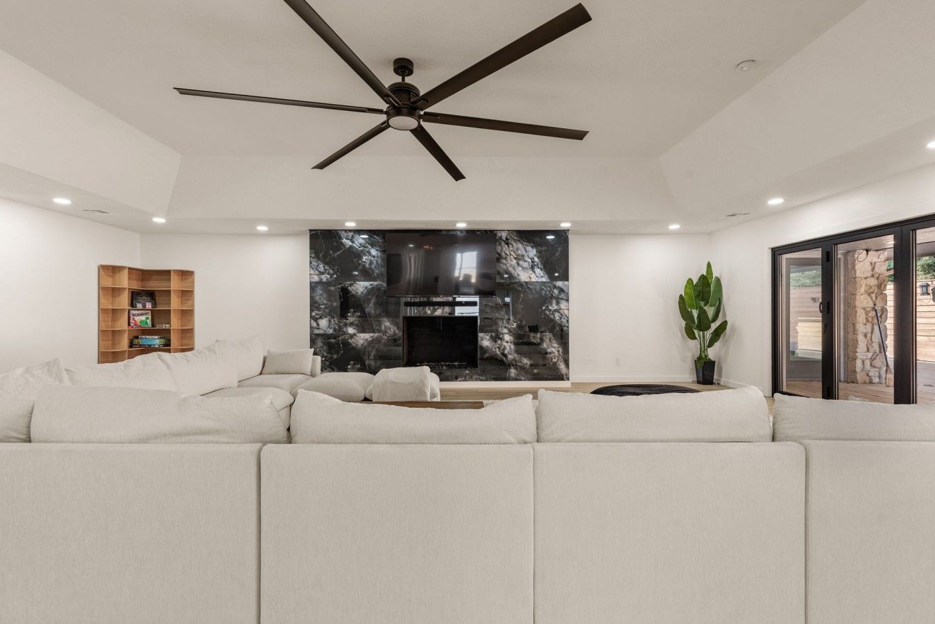 Un salon moderne avec un canapé d’angle, un téléviseur à écran plat, une cheminée et un ventilateur de plafond.