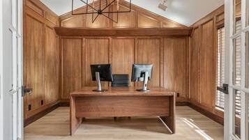 A room with wooden paneled walls, a desk with two monitors, and a modern chandelier.